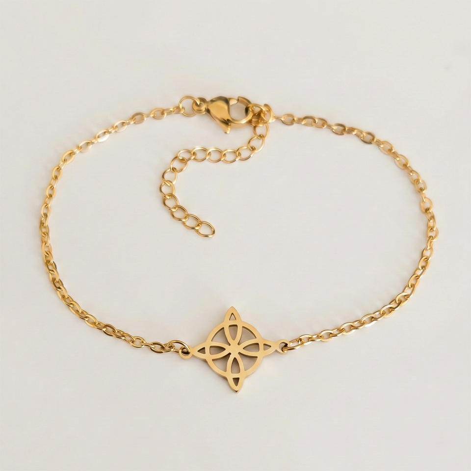 Armband i guldfärgat rostfritt stål med en häxknut, fotograferat mot en vit bakgrund.