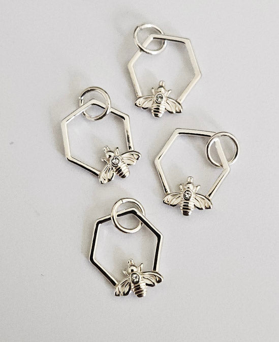 Fyra likadana silverhängen formade som hexagoner med små bin, liggandes på en ljus bakgrund.