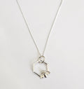 Närbild på ett silverhalsband med ett hängsmycke format som en sexkantig hexagon. I botten av ramen sitter ett litet, detaljerat bi i silver med en klar sten på ryggen.