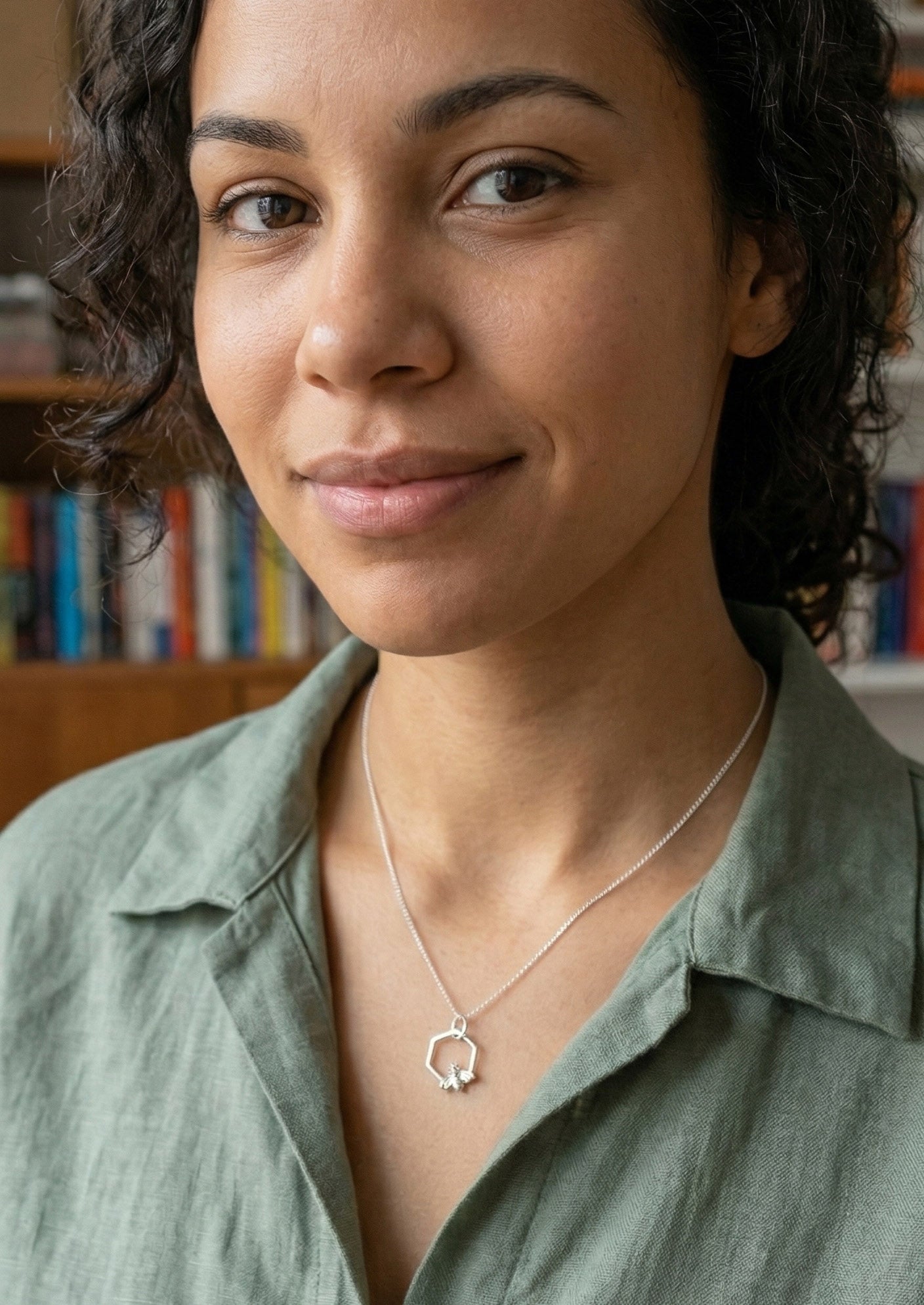 En kvinna som bär ett stilrent silverhalsband. Hänget är format som en hexagon med ett litet bi i nederkanten.