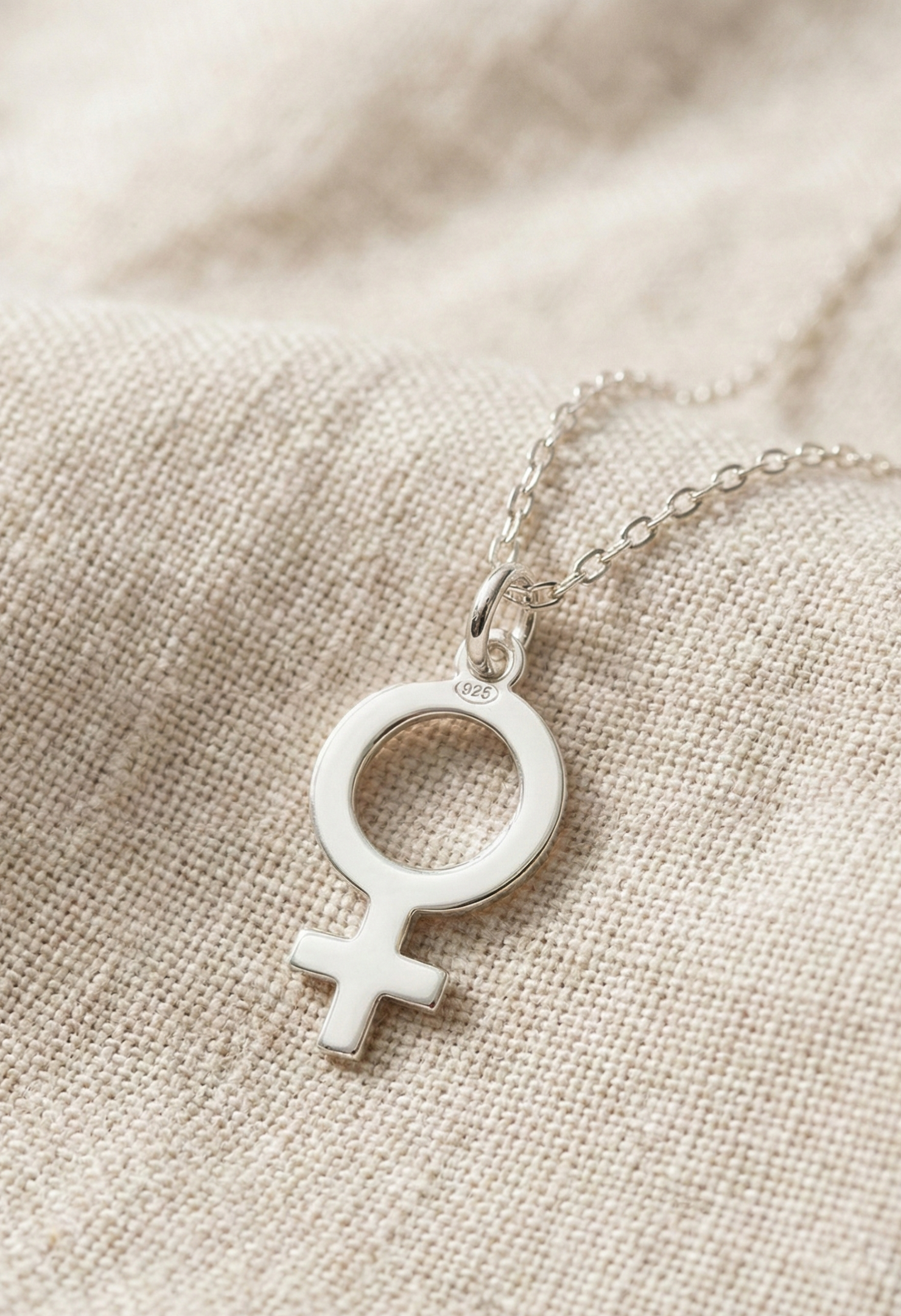 Närbild på feministsymbol hängsmycke i äkta silver på beige tygbakgrund